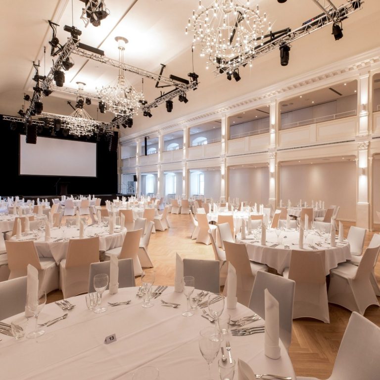 Der leere große Saal in Reihenbestuhlung mit aufgebauter Bühne und blauer Bühnenbeleuchtung.